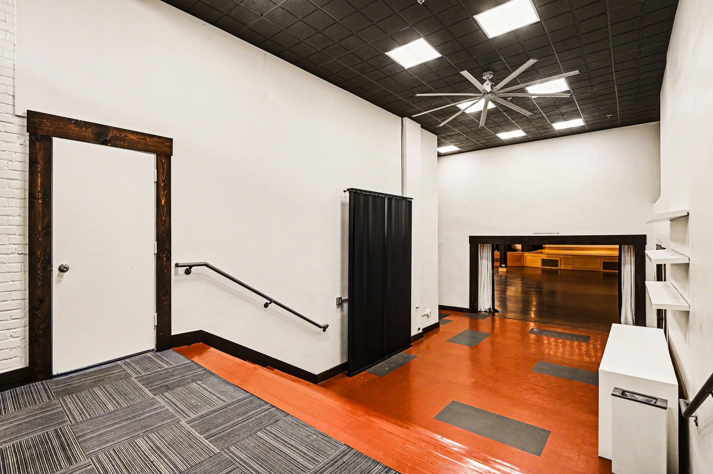 Nippon kan theatre, seattle, washington, event space, wedding, Interior view of a room with a staircase, white walls, black ceiling with recessed lighting, and a mix of carpeted and wooden floors.