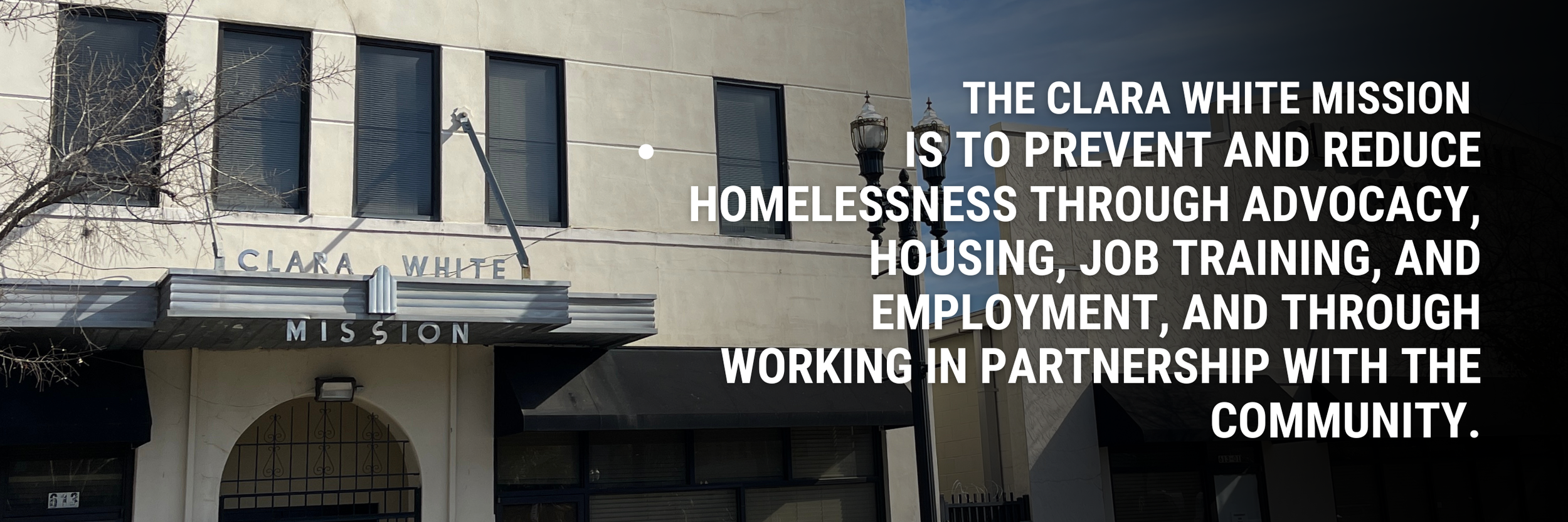 The exterior of the Clara White Mission building with a sign that reads 'Clara White Mission' above the entrance. Overlaid text states the mission's goal to prevent and reduce homelessness through advocacy, housing, job training, employment, and community partnership.