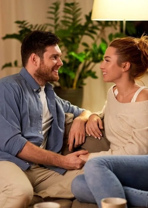 Man and woman sitting on a couch in a marriage coaching appointment holding hands and smiling at each other.