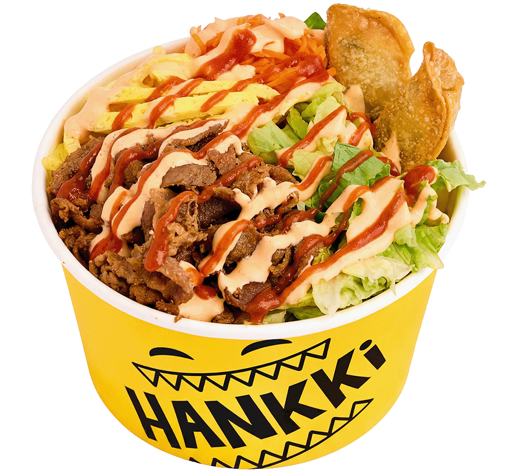 Bowl of Asian noodle salad topped with sliced beef, drizzled with sauce and mayonnaise, alongside shredded carrots, lettuce, and a fried dumpling. The yellow bowl features a smiley face and the text "HANKKKI."