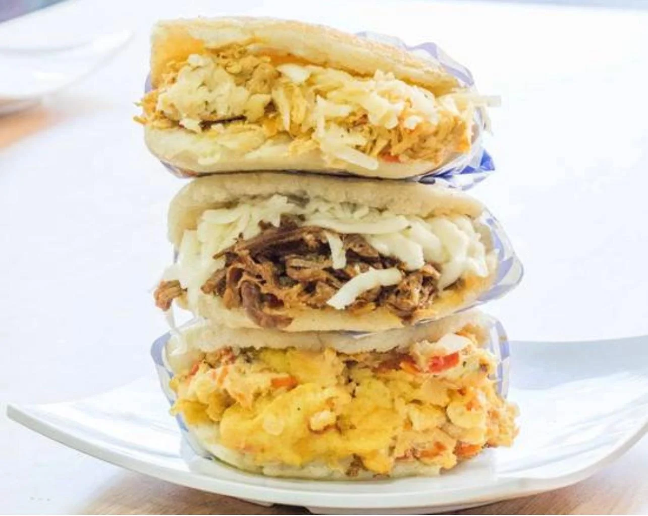 Stacked breakfast sandwiches with various fillings on a white plate.