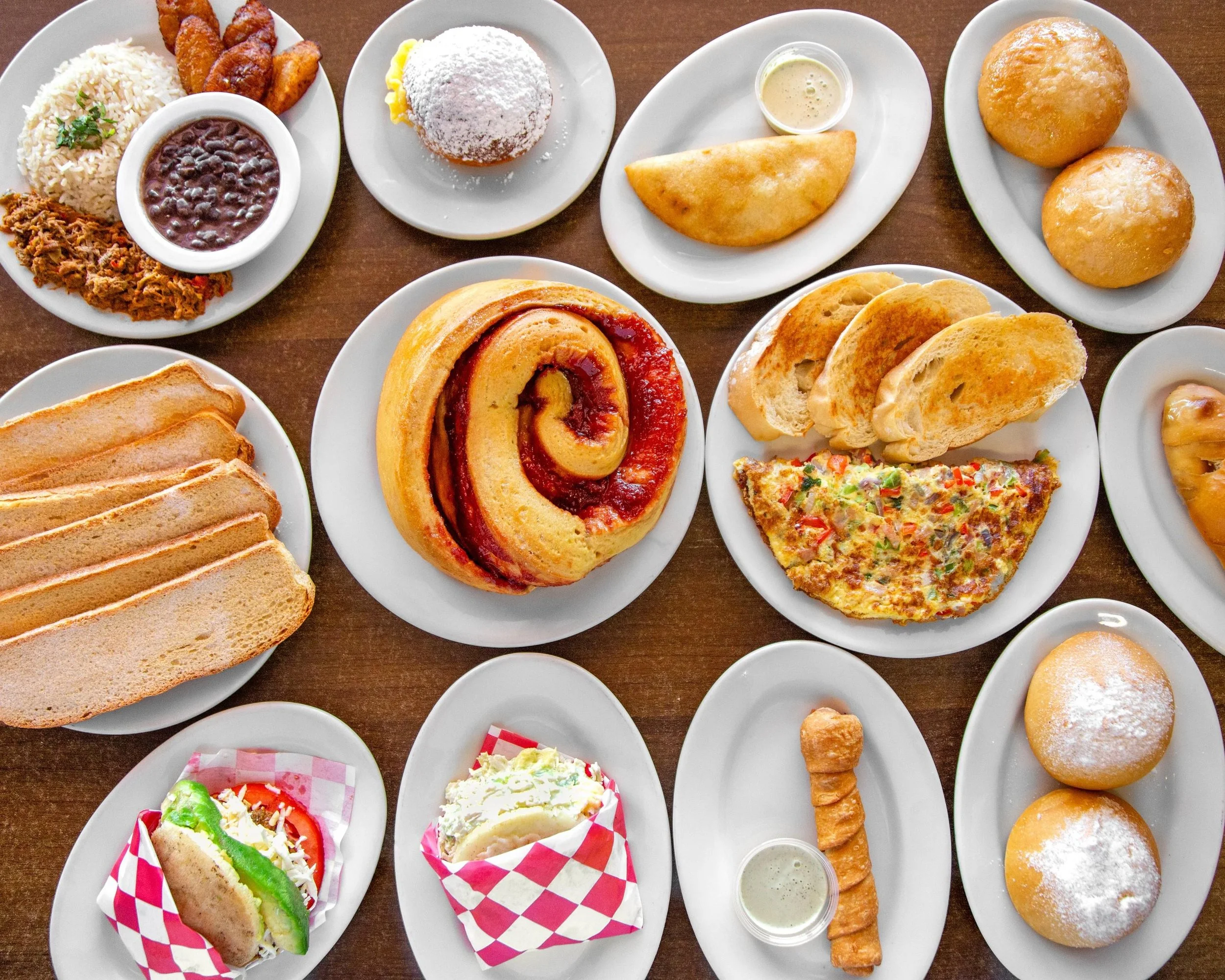 Assorted dishes including bread, pizza, cinnamon roll, fried chicken, rice, beans, a sandwich, desserts, and pastries on white plates.