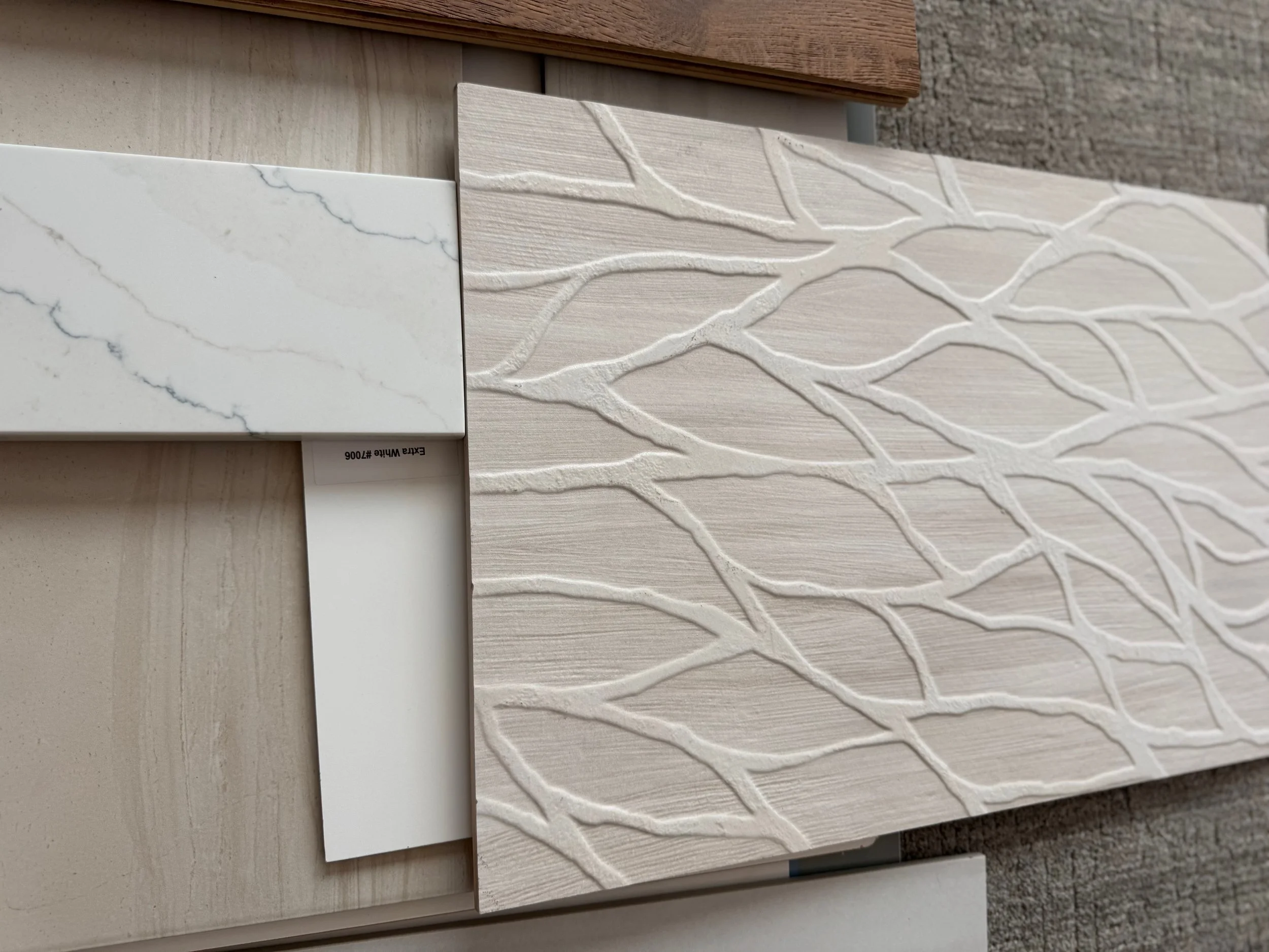 Close-up of sample tiles with marble and wood textures, featuring a decorative 3D white leaf pattern on a beige background.