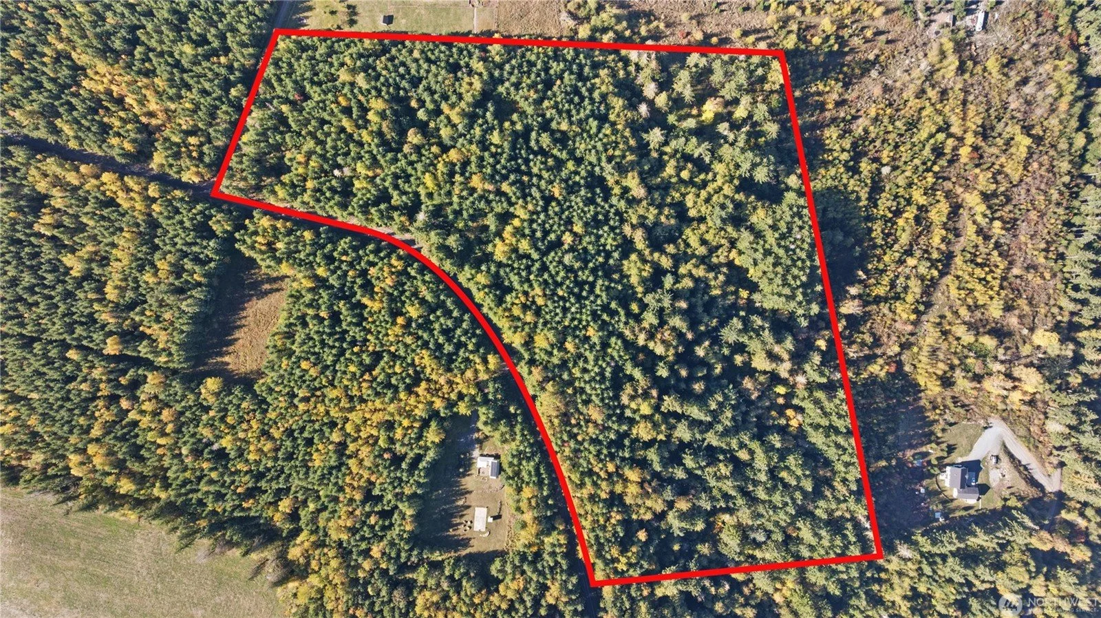 An aerial view of a wooded area with a red boundary outline marking a large plot of trees and land. There are some small structures visible near the bottom and right edges of the image, with surrounding trees and open grassy areas.