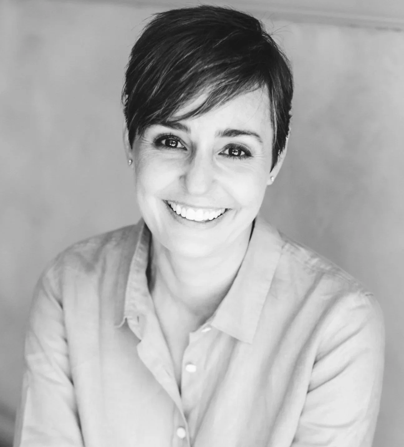 Black-and-white portrait of a smiling woman with short hair, wearing a collared shirt, looking directly at the camera.
