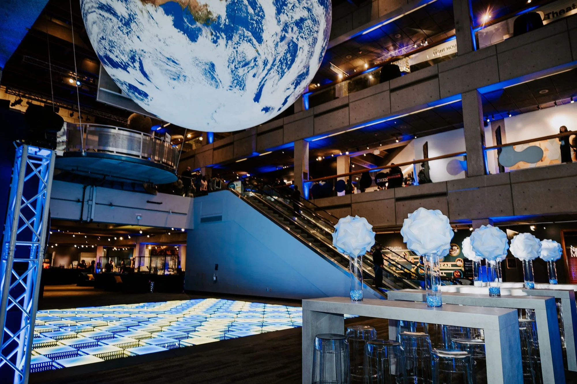 LED dance floor, cement share tables, and white florals under the giant Earth in the Museum of Science Blue Wing for a corporate awards gala and 40th anniversary, produced by Siagel Productions