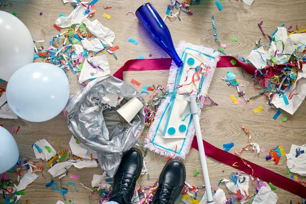 Confetti, ribbons, and cleanup supplies scattered across the floor after a party, showing the hidden time cost of planning an event yourself