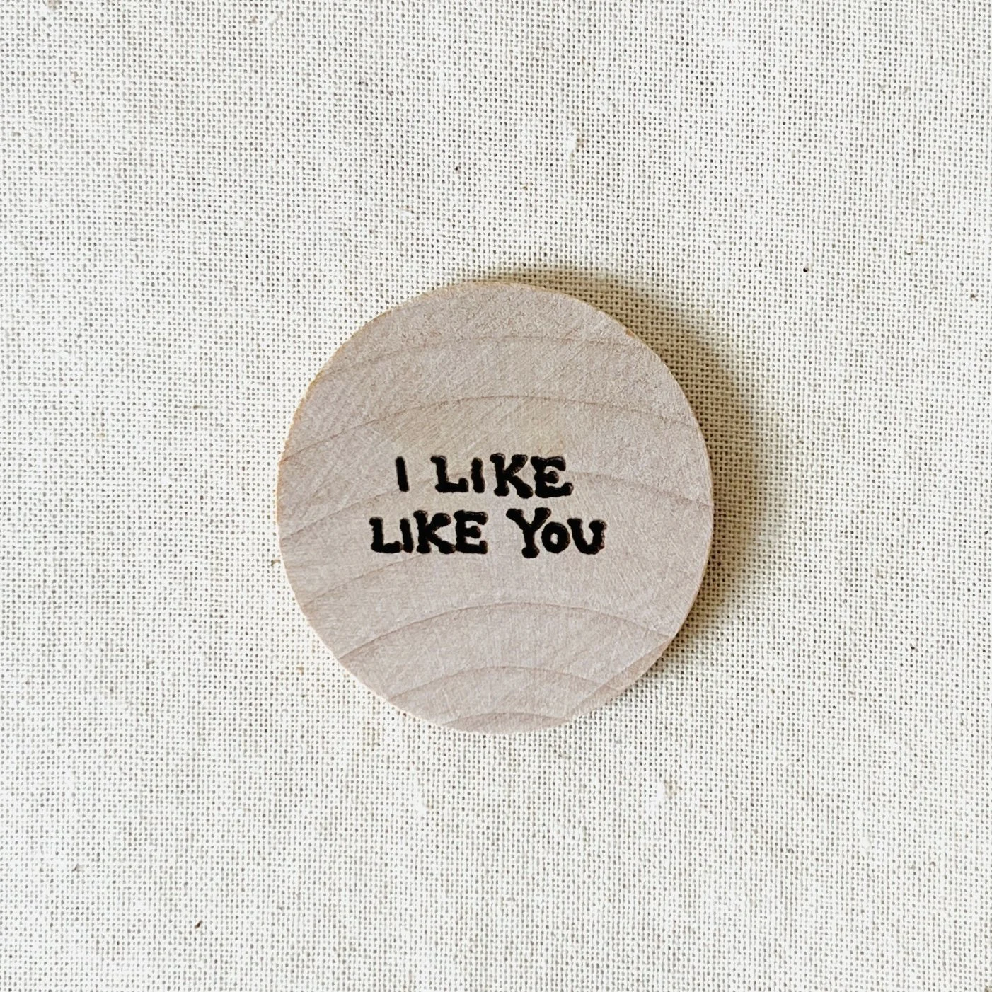Round wooden compliment coin with the phrase 'I LIKE LIKE YOU' written in black text on a white background.