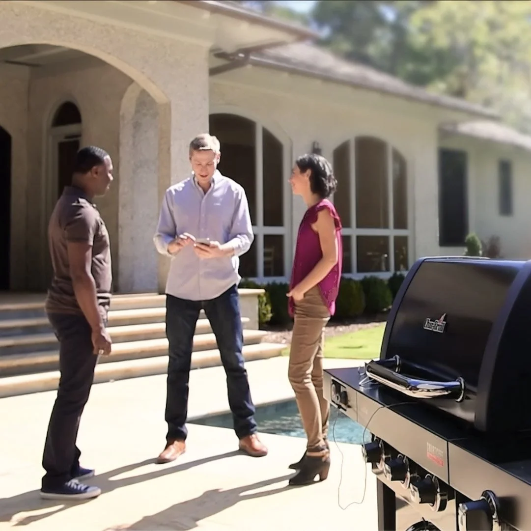Lifestyle photo of three people at a backyard cookout. They're using a smartphone app to control the BBQ grill. Photography by Chris Wulff