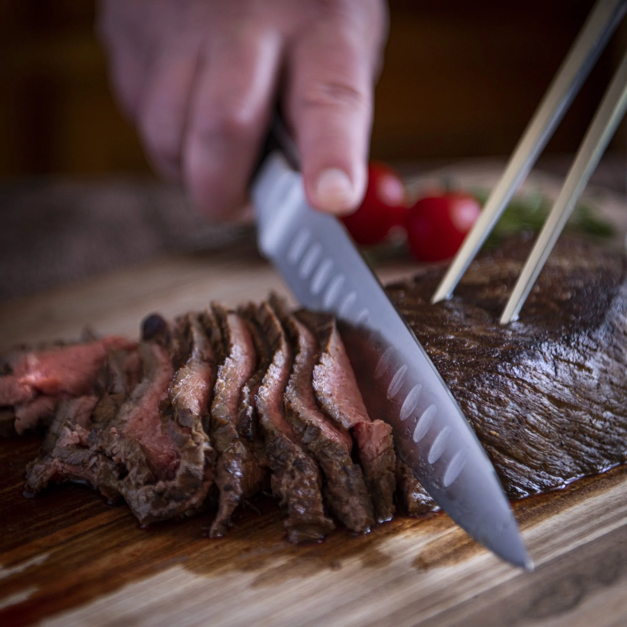 Lifestyle product photo of a stainless steel carving set cutting a perfectly cooked steak. Photography by Chris Wulff
