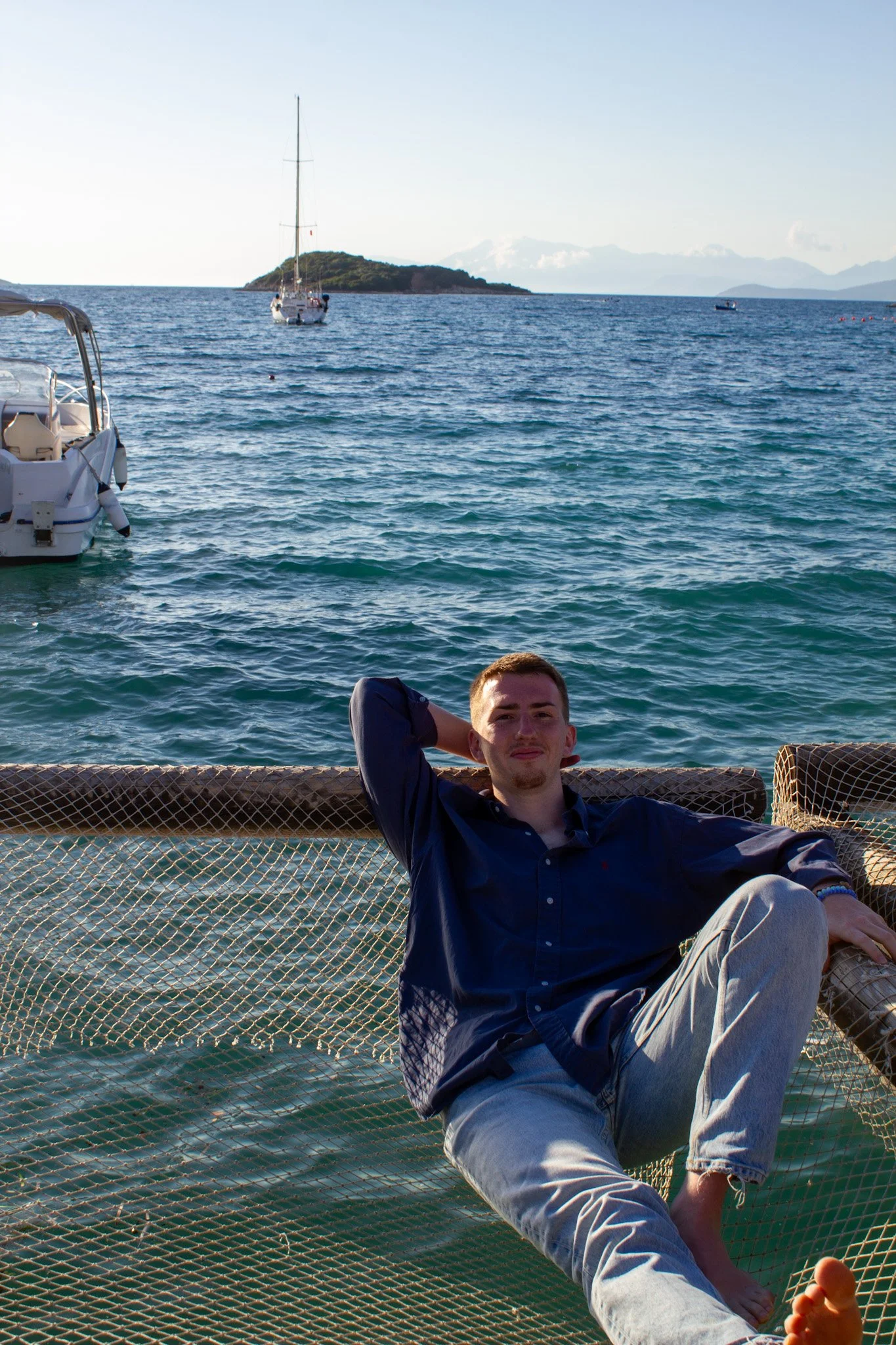 Max aesthetics picture on net lounger over sea with boats in background, Ksamil, Albania
