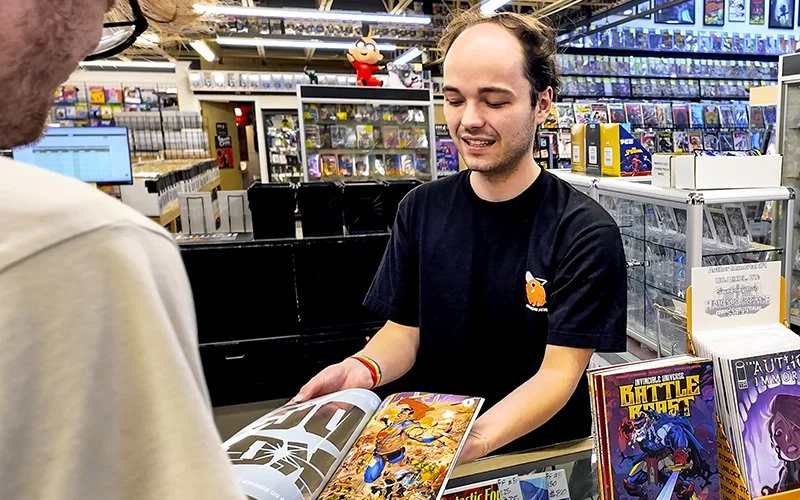 Employee displaying a comic book to a customer within the store