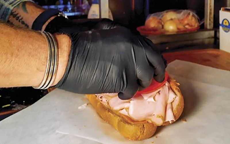 Person preparing a turkey and tomato sandwich on a hoagie style bread bun