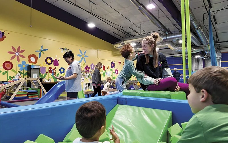 Kids Gym employee facilitating play with a couple of young children in a foam pit