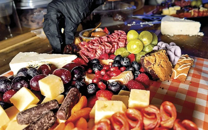 Person preparing a charcuterie platter featuring fresh berries, smoked meats, various cheeses, and biscotti.