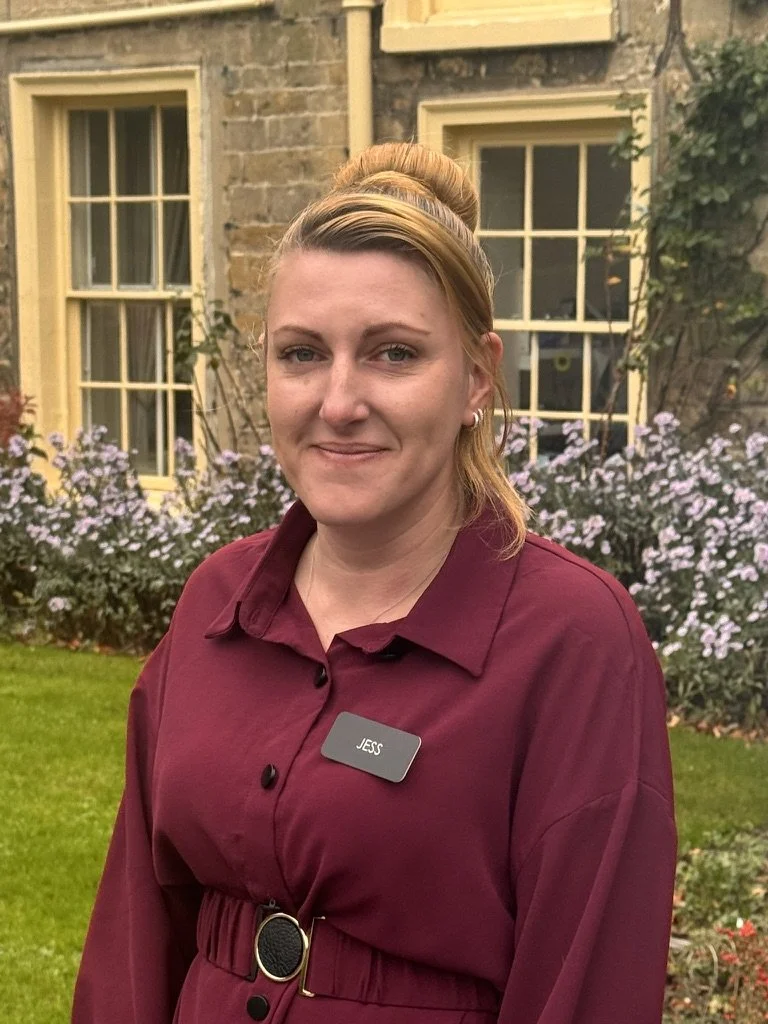 Female with short blonde hair, wearing a floral black and white top