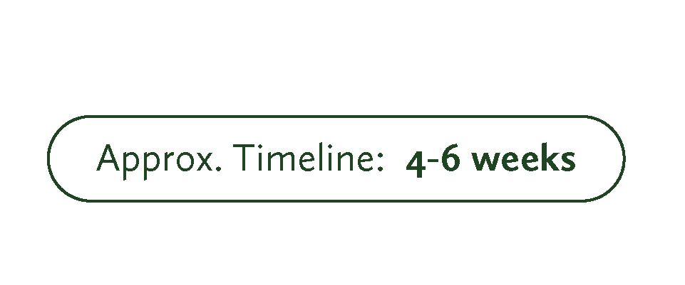 A woman with glasses and dark hair pulled back, holding a paintbrush in her right hand and a cup in her left, painting a colorful mural of a yellow train with cartoon characters and food banners on a yellow wall.