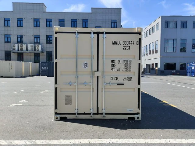 Stacked shipping containers in various colors including pink, blue, green, red, orange, and brown, arranged in a grid at a shipping yard.