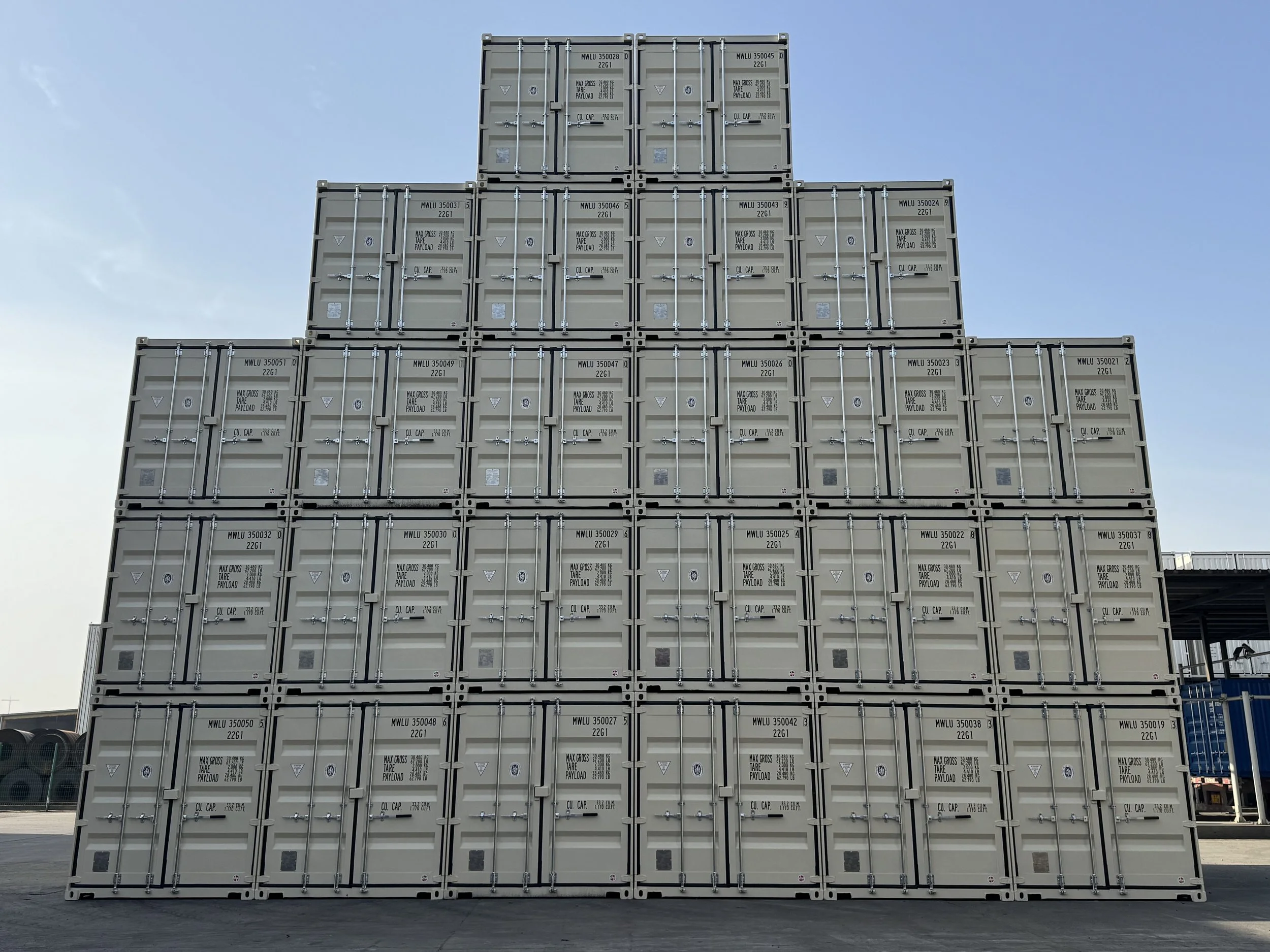 Stack of beige cargo shipping containers arranged in a pyramid shape against a blue sky.