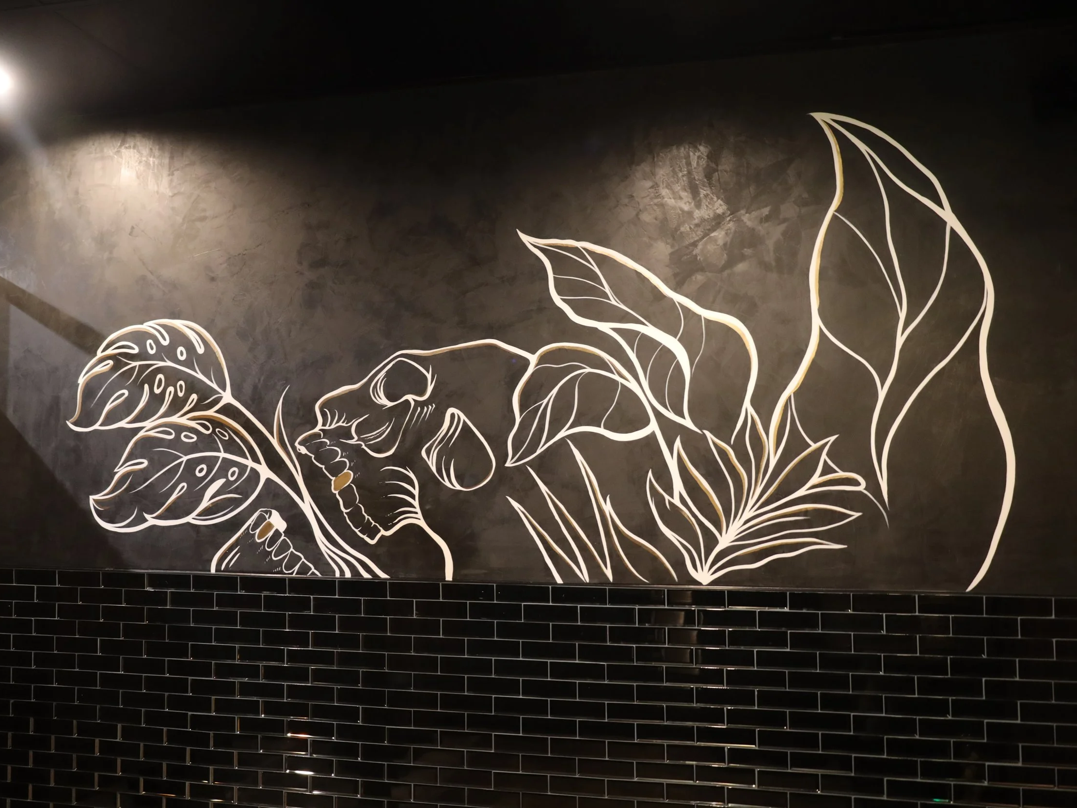 Minimalist white line art botanical mural on a dark textured wall, showcasing flowing leaves and organic forms.