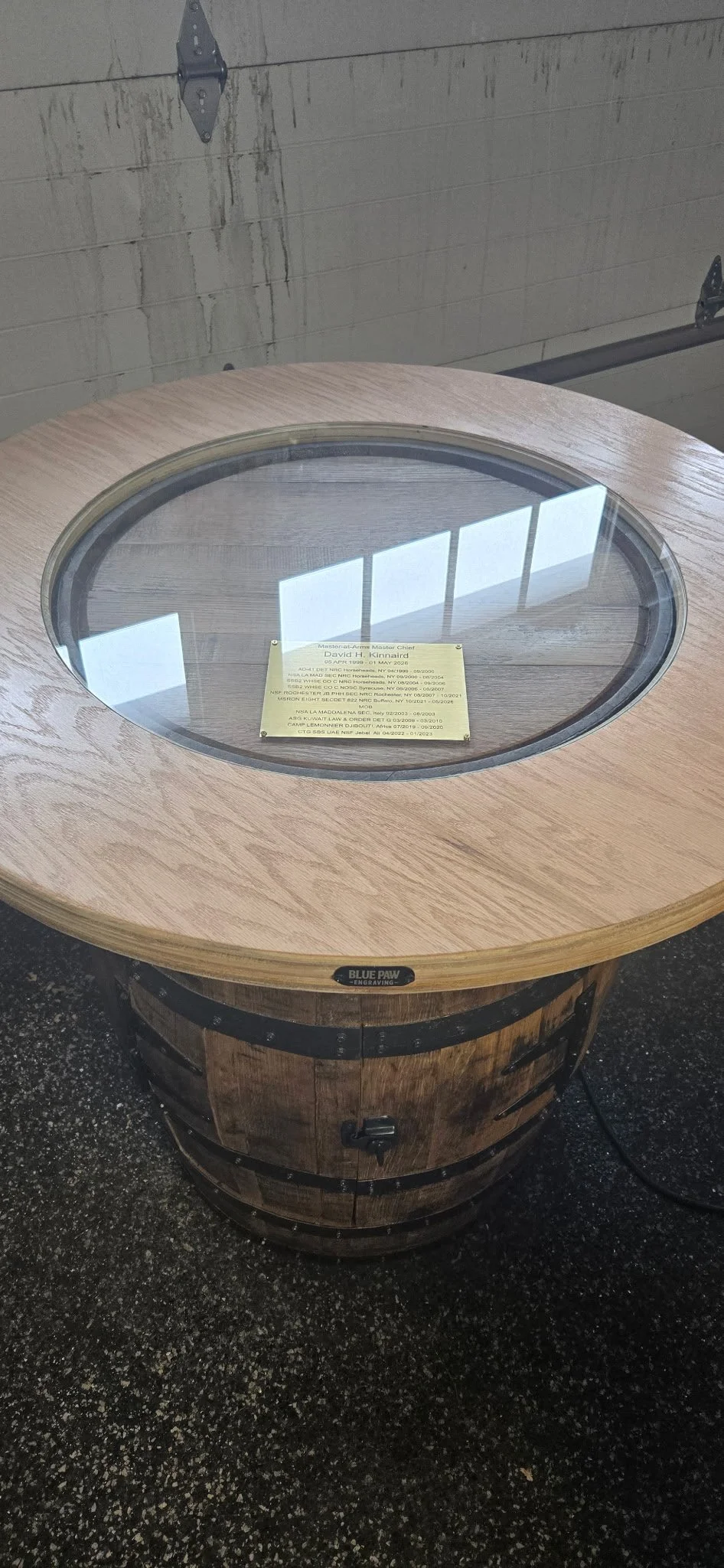 Whiskey barrel table with large round wood and glass top. Engraved plaque under the glass.