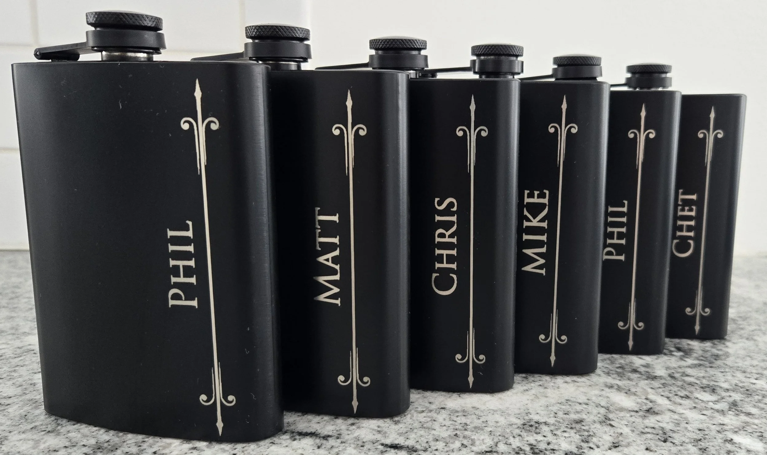 Black flasks engraved with names of groomsmen for wedding party gifts