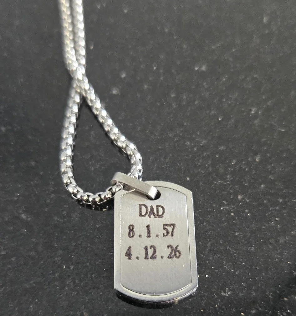 Silver dog tag engraved with Dad and date of birth and death