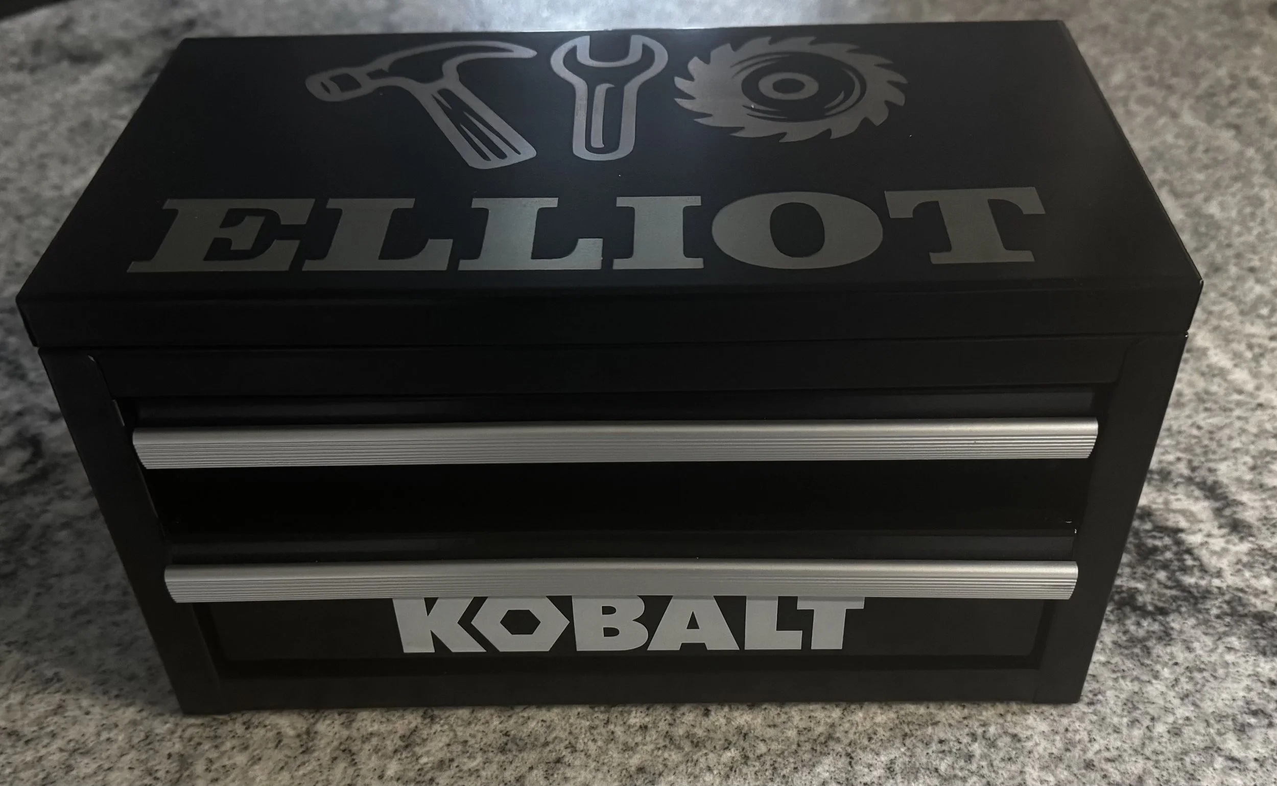 Childs black and silver Kobalt toolbox engraved with pictures of tools and the name Elliot