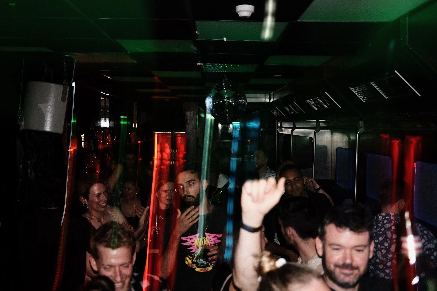 People dancing and socializing at a party with colorful lights and a disco ball in a dark room.