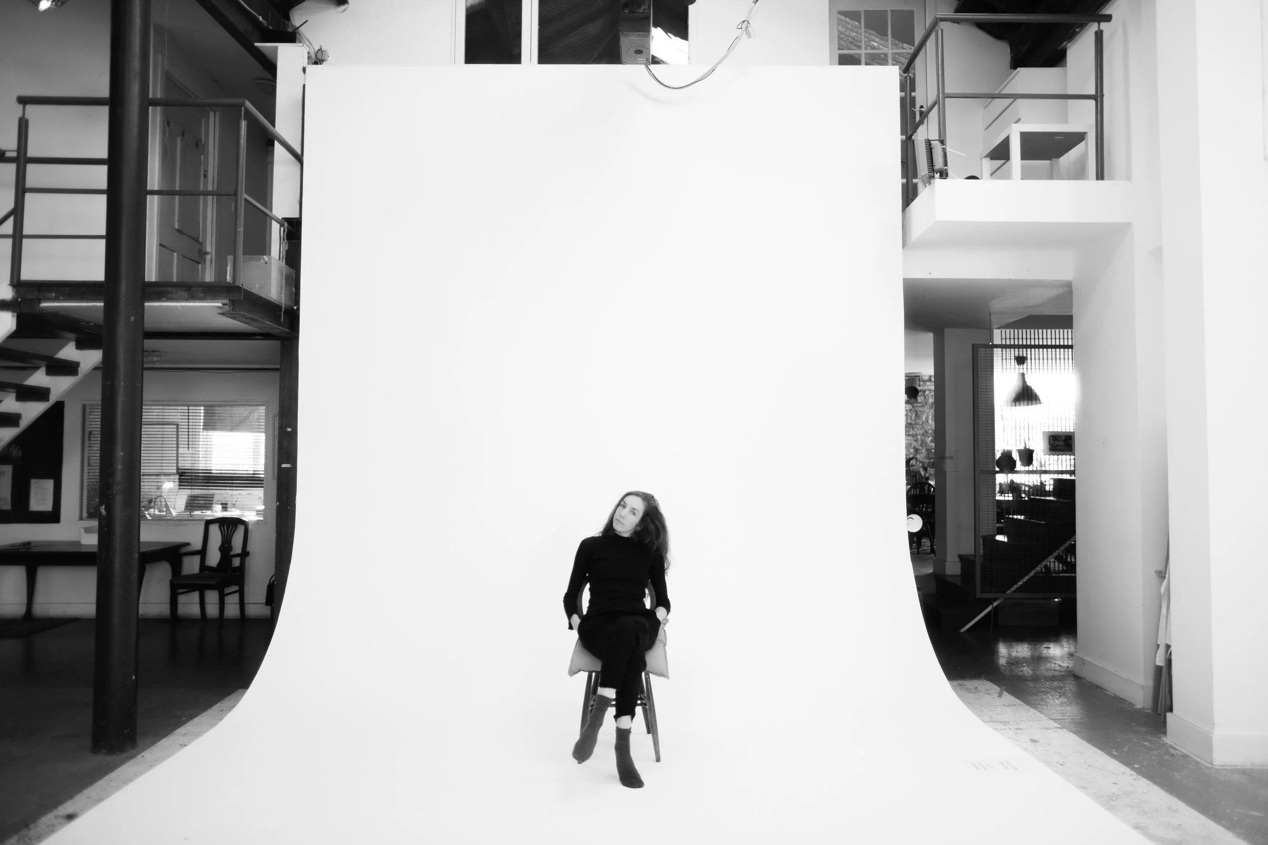 Woman sitting on a chair in a photography studio with a white backdrop.