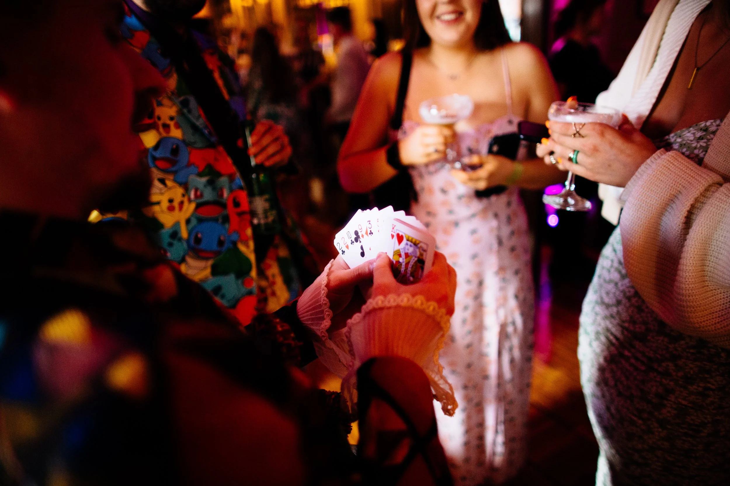 People at a social event holding drinks and playing cards, with a woman smiling in focus.