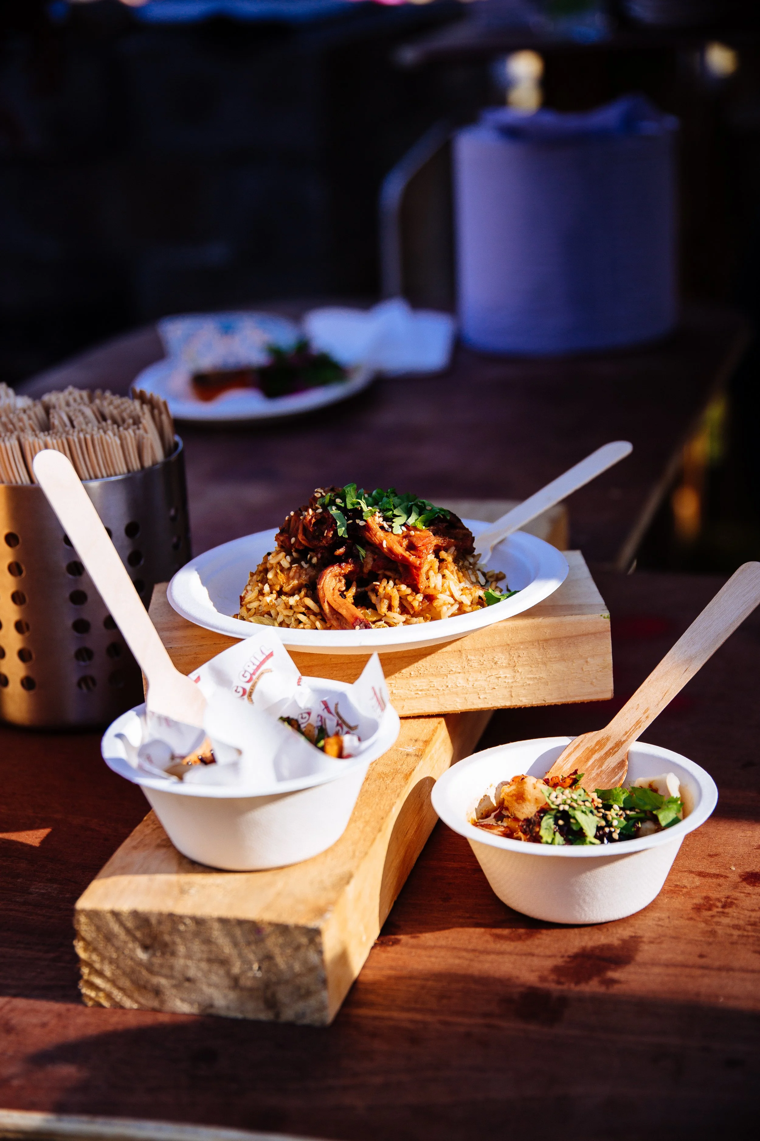 Close-up of Asian-style dishes on a wooden serving tray, including rice mixed with meat and vegetables, small bowls of sauce and salad, with chopsticks nearby, on a wooden table.