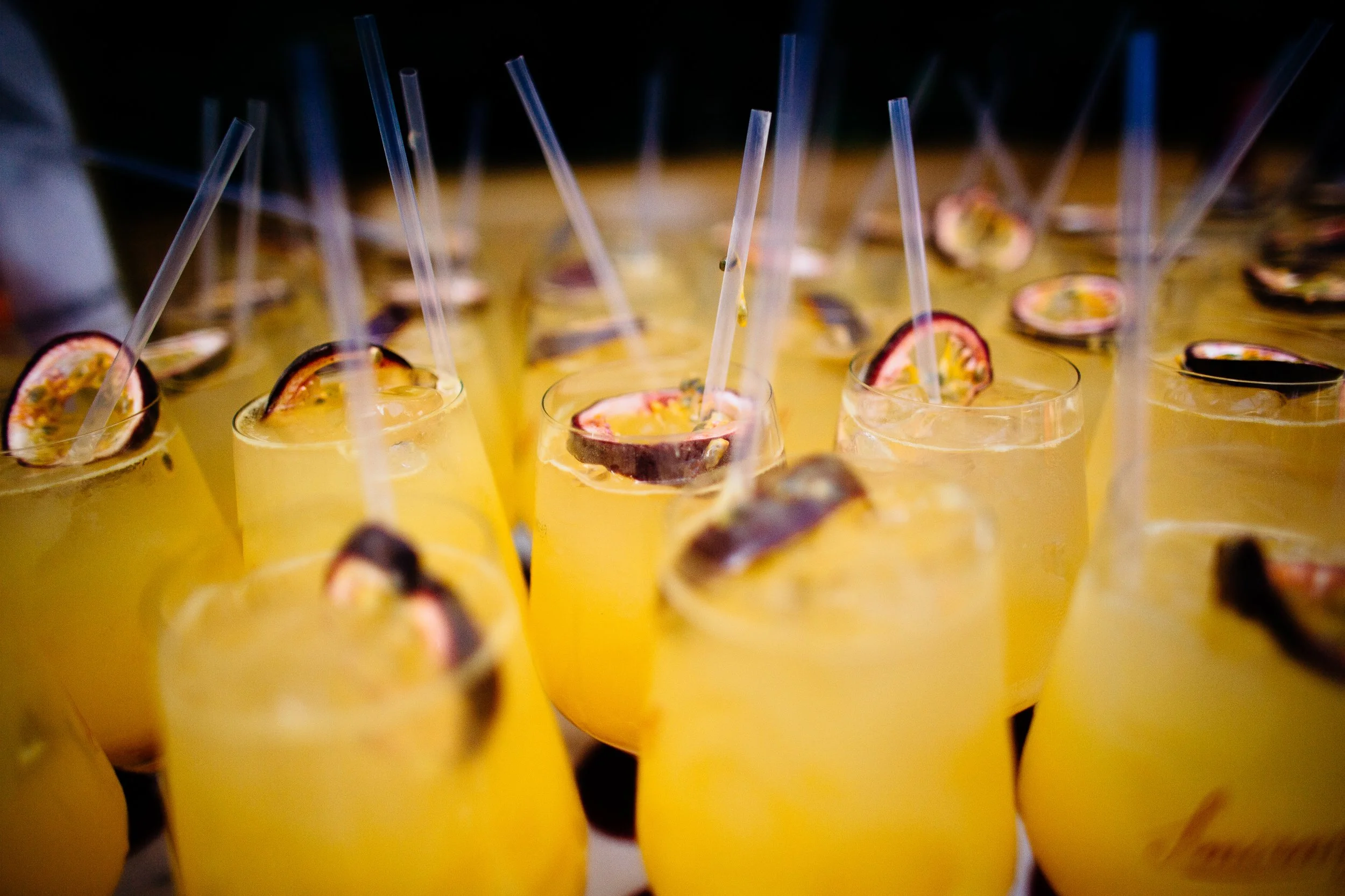 Multiple yellow drinks topped with passion fruit halves and clear straws.
