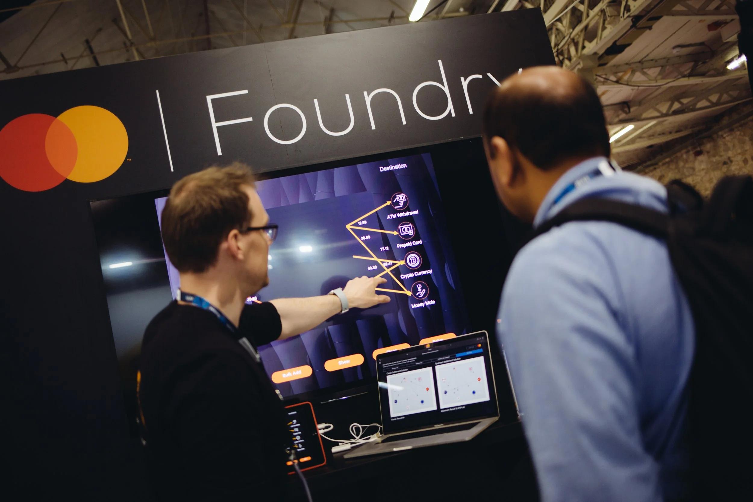 Two people are looking at a digital screen displaying cryptocurrency information at a Foundry booth.