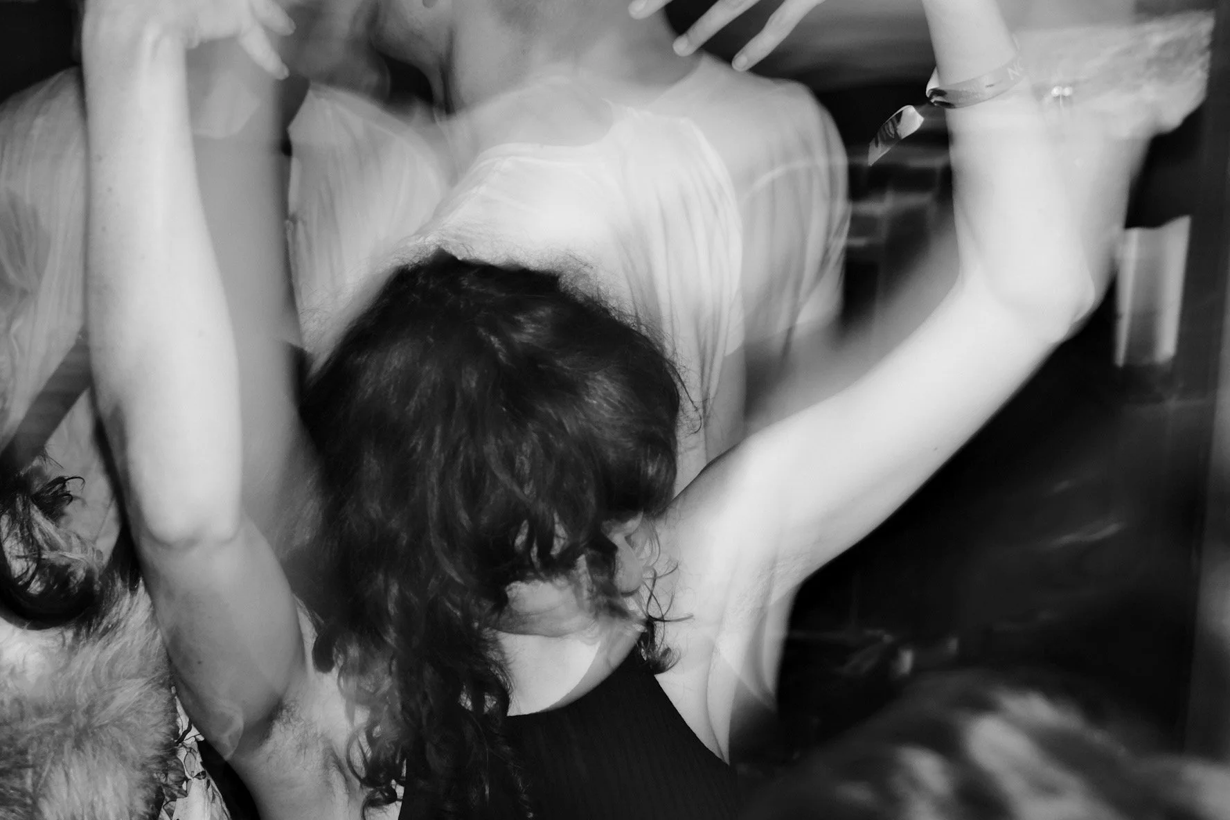 Black-and-white photo of a person lying on a table with their head tilted back, arms extended, and hair tousled, in a possibly artistic or theatrical setting.