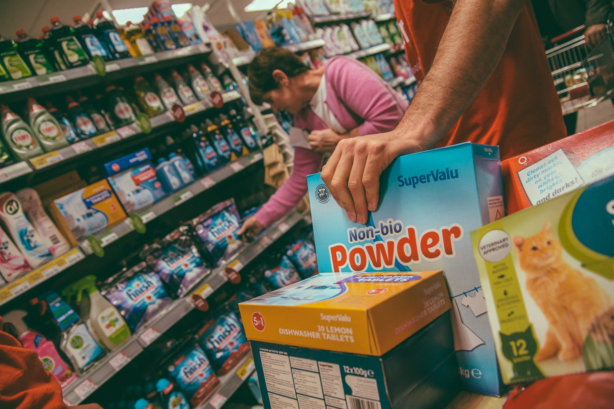 Close-up of a person holding a box of SuperValu Non-bio Dishwasher Powder on a store shelf with other cleaning products visible in the background.