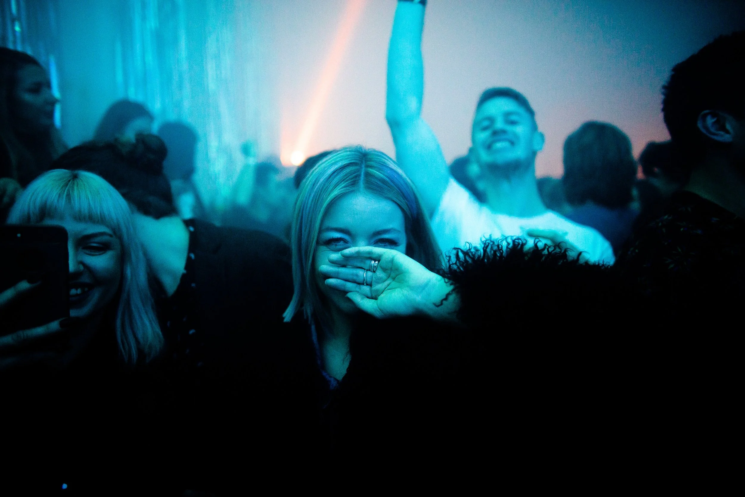 People at a party or concert, smiling and enjoying themselves, with blue and purple lighting effects.