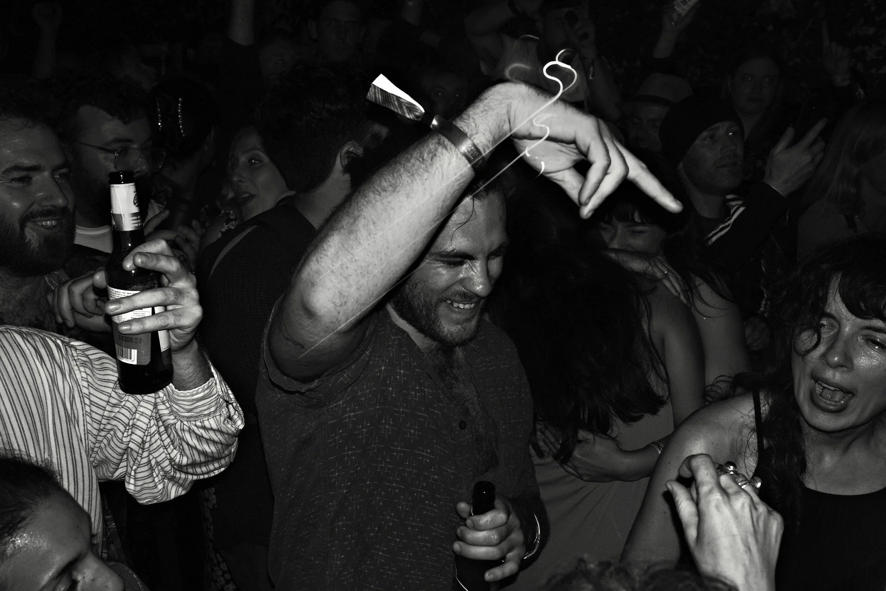 People dancing and celebrating at a party, some holding drinks, with joyful expressions.