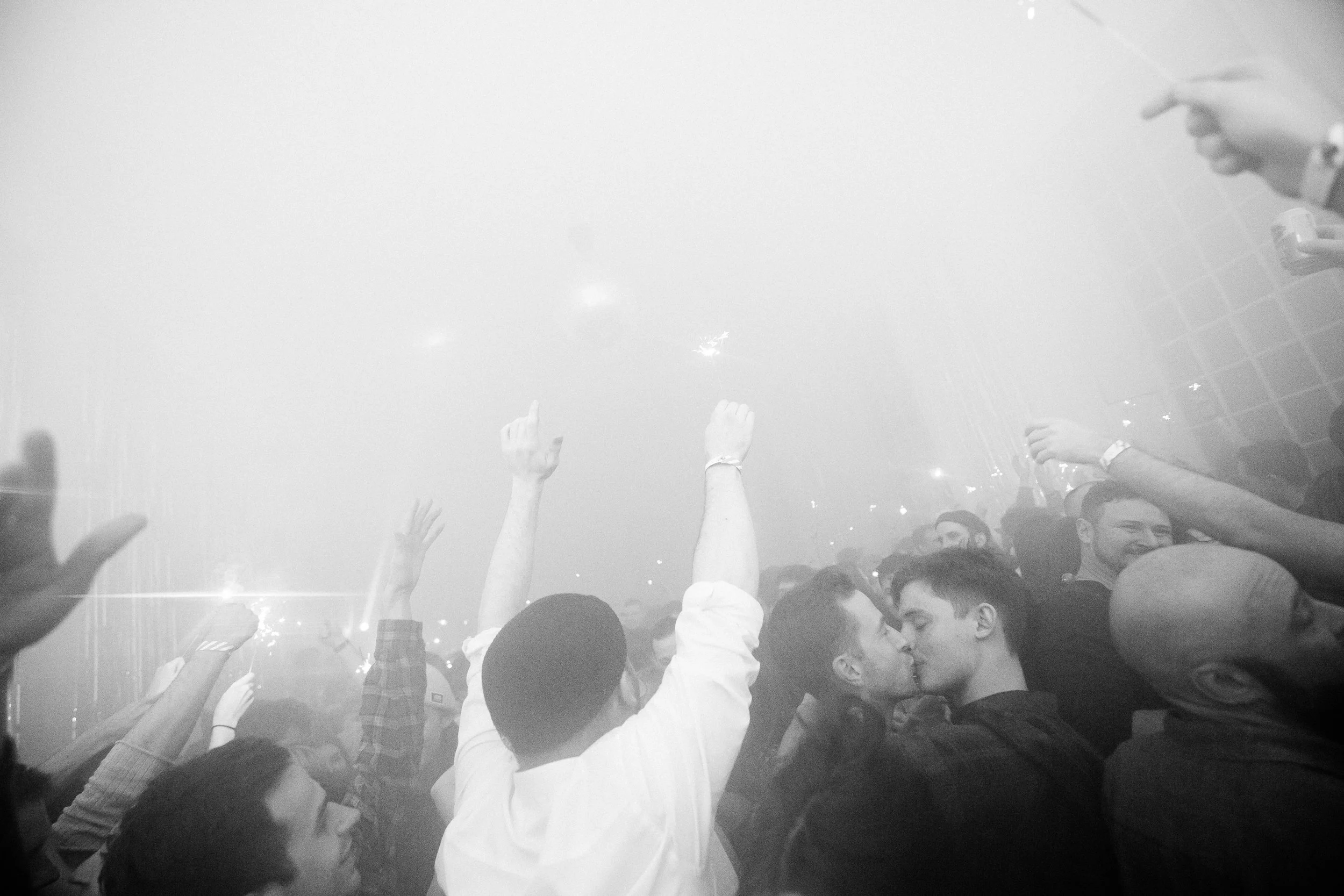 A crowd of young people at a concert or festival, raising their hands and enjoying the live music. The image is in black and white.