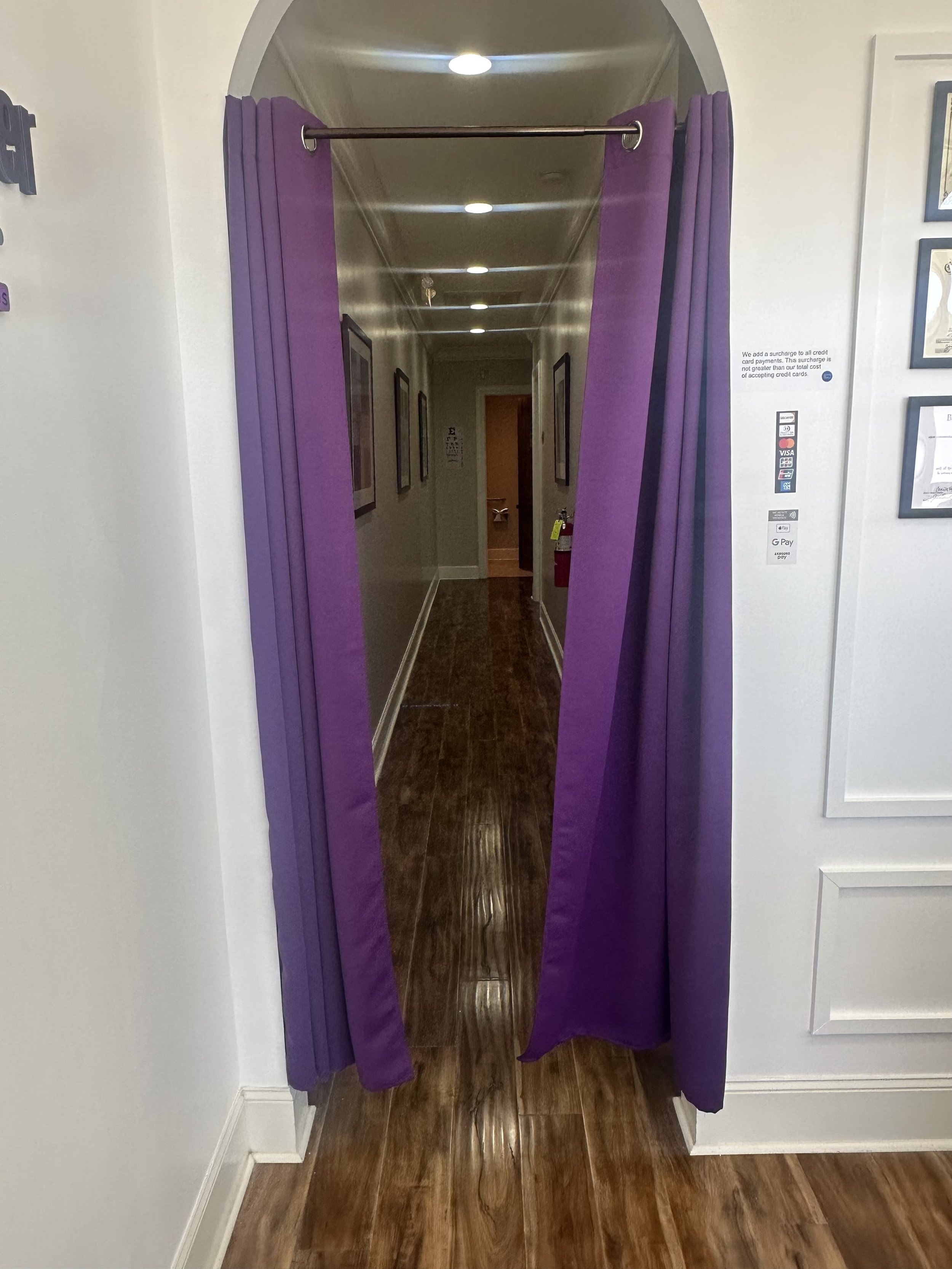 Purple fitting room curtain hanging in a hallway with wooden flooring and framed pictures on the walls.