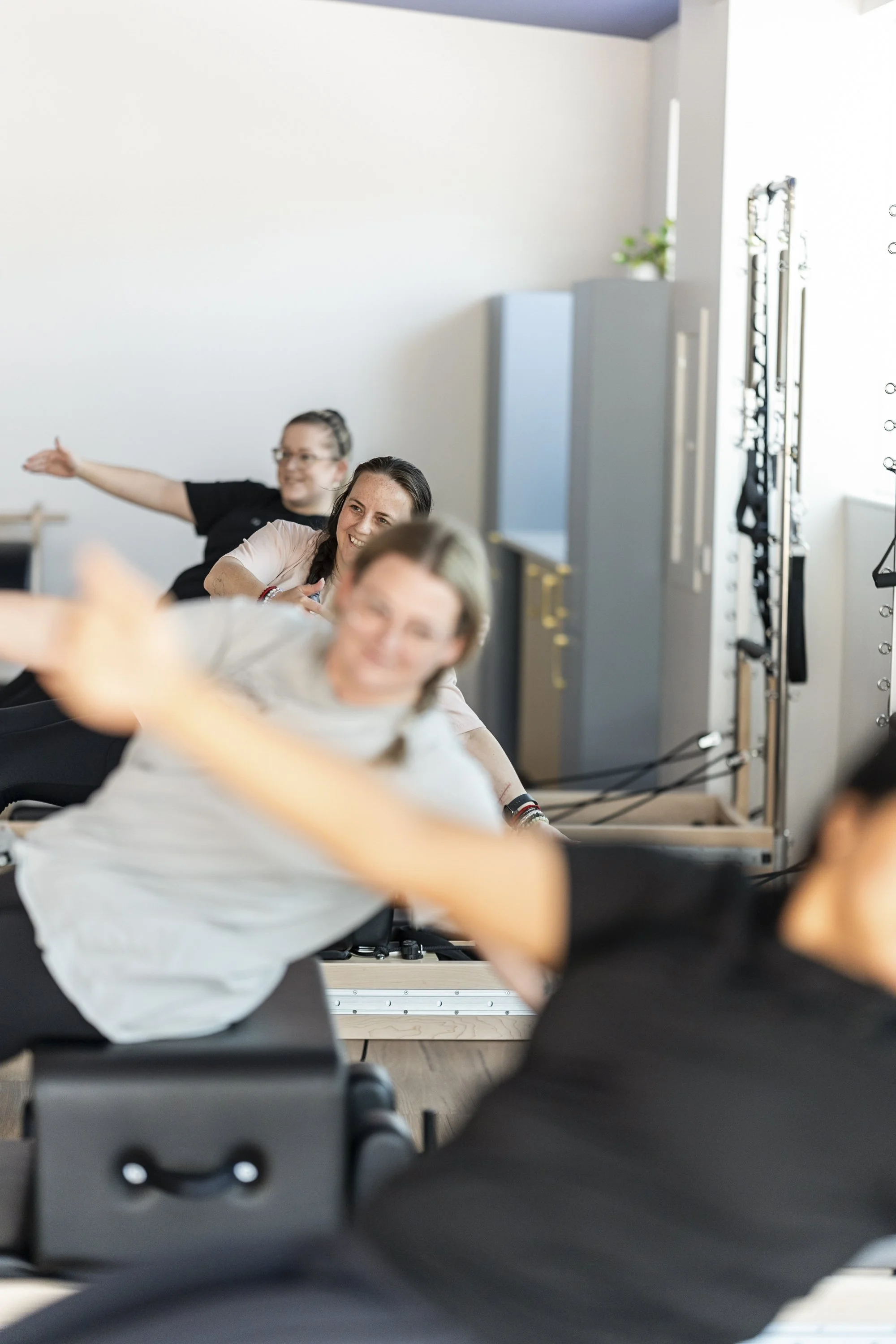 People participating in a fitness class, stretching on chairs in a bright room with a minimalist decor, including a plant and gym equipment.