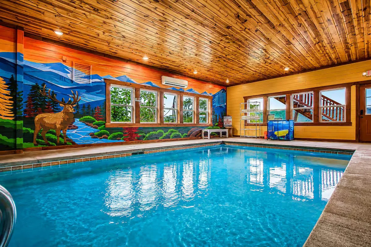 Custom indoor pool mural featuring the Smoky Mountains, elk, bear, and flowing stream in a cabin in Pigeon Forge, Tennessee.