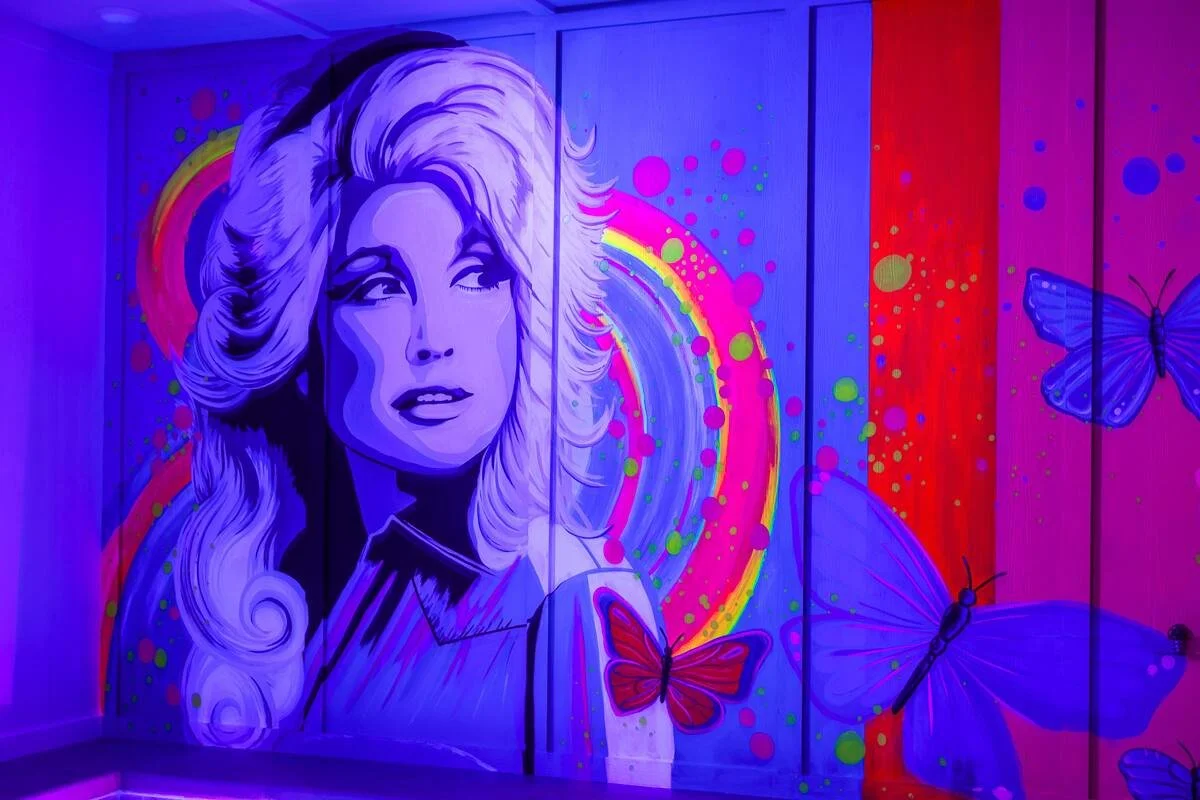 Vibrant neon-style Dolly Parton portrait mural with colorful butterflies in a Sevierville, Tennessee cabin.