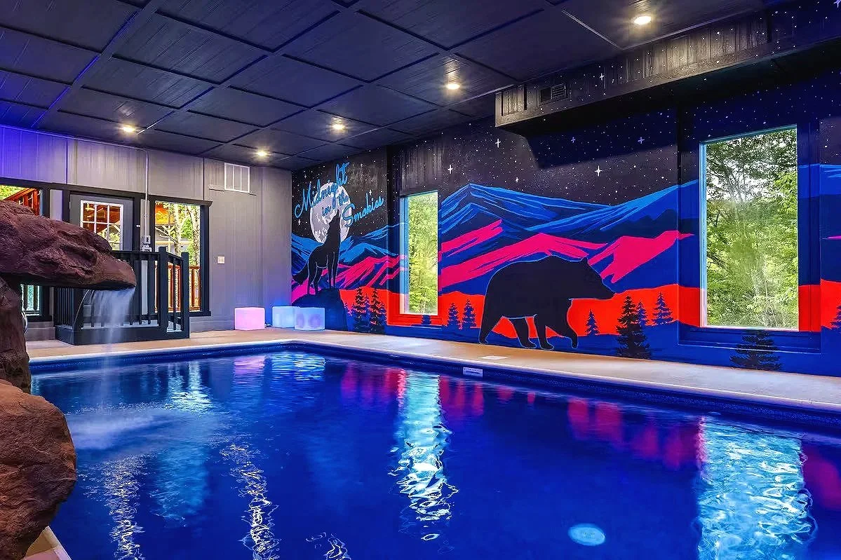 Neon indoor pool mural featuring the Smoky Mountains, starry sky, bear, and howling wolf in a cabin in Sevierville, Tennessee.
