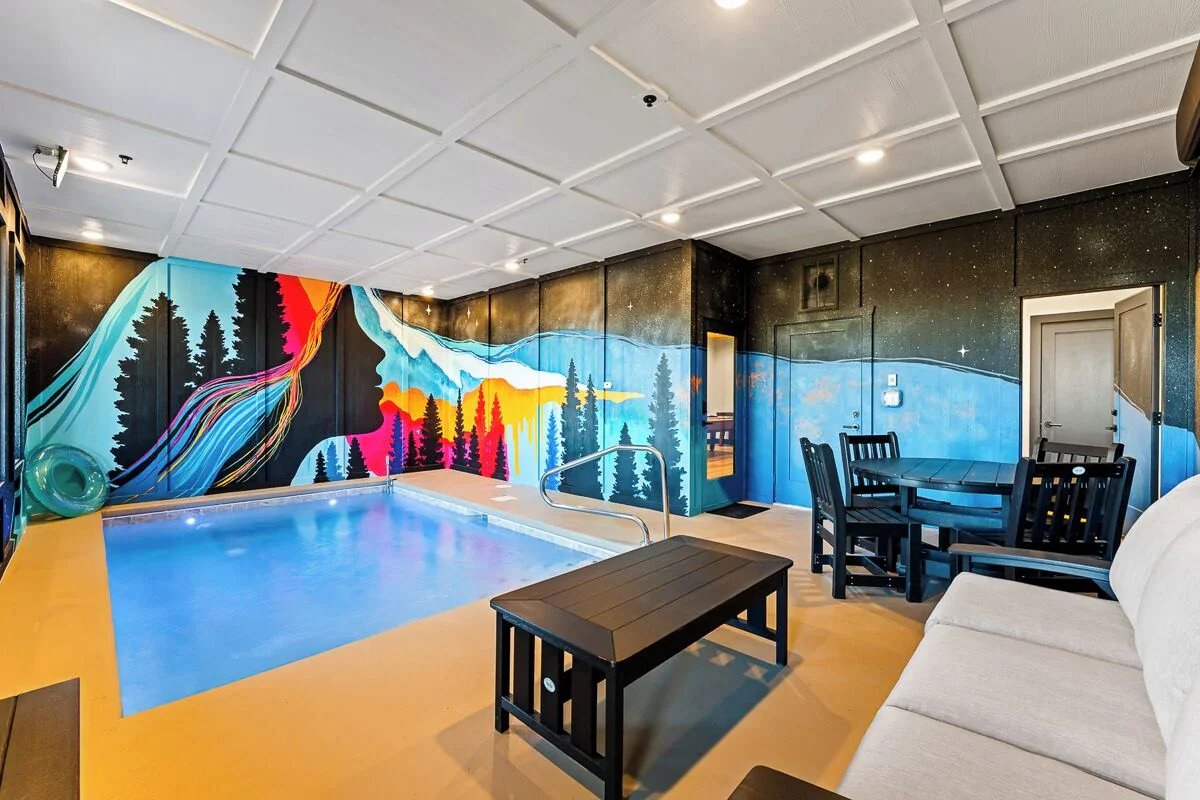 Vibrant neon-style mural of glowing mountains and pine forests in a Smoky Mountains cabin pool area.