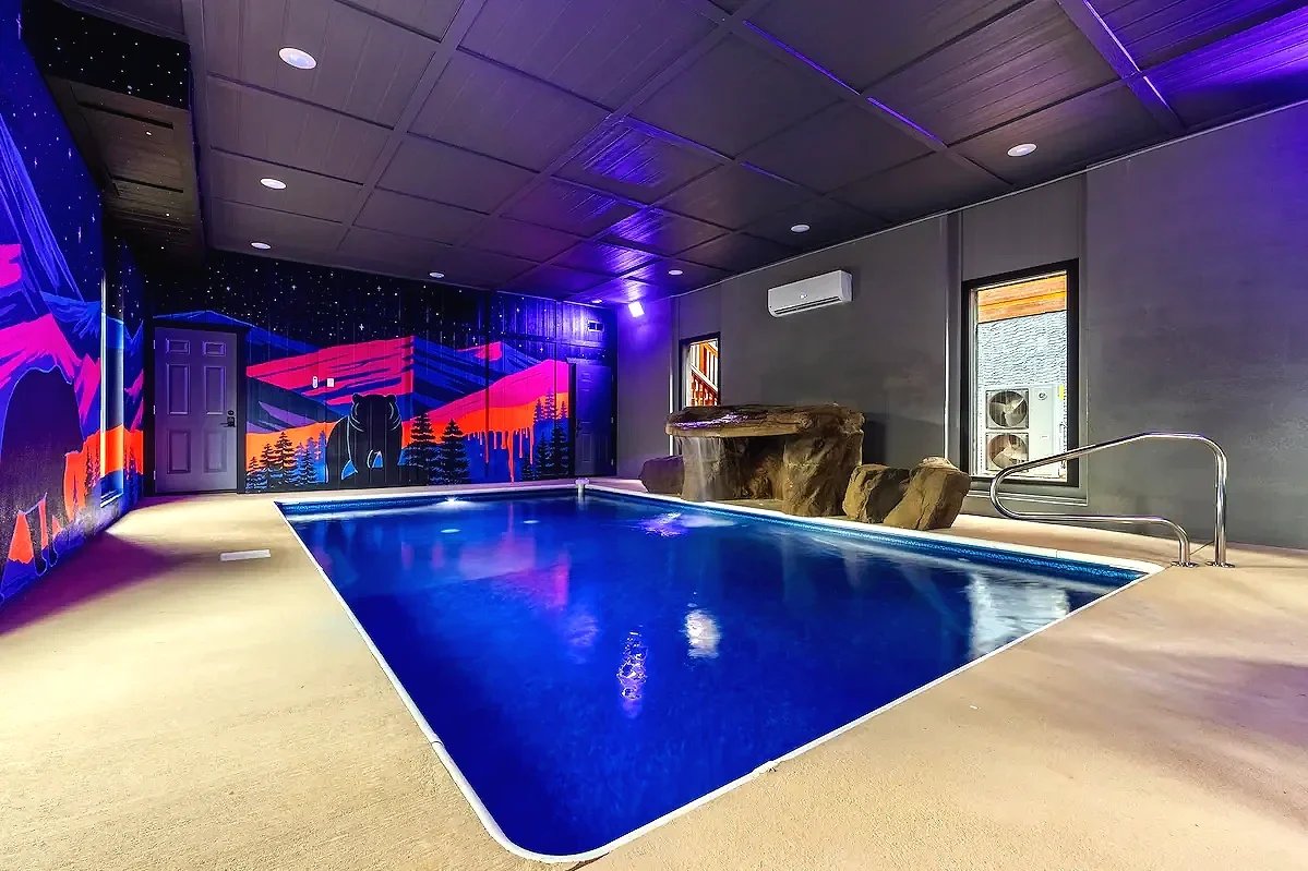 Neon indoor pool mural featuring the Smoky Mountains, starry sky, bear, and howling wolf in a cabin in Sevierville, Tennessee.