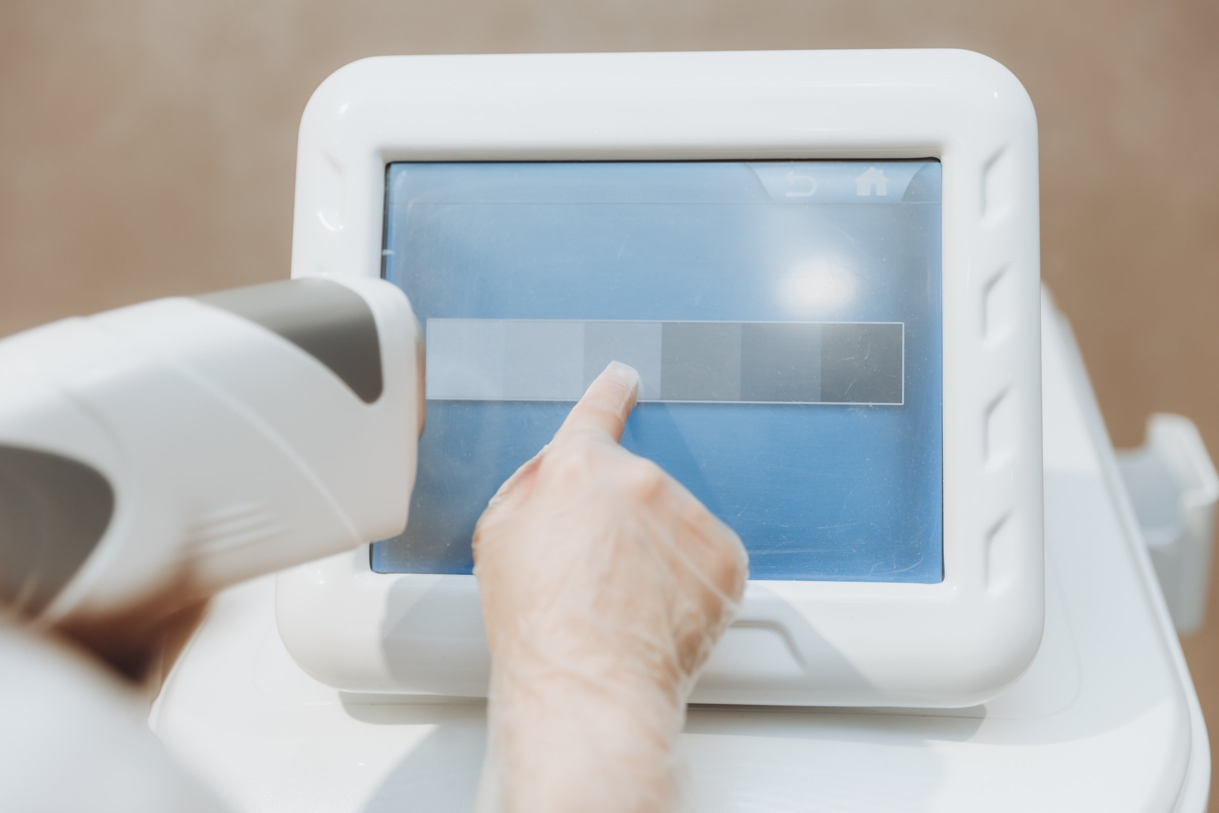 Person wearing gloves using a touchscreen device, possibly a medical or laboratory instrument, with a gun-like attachment pointed at the console.
