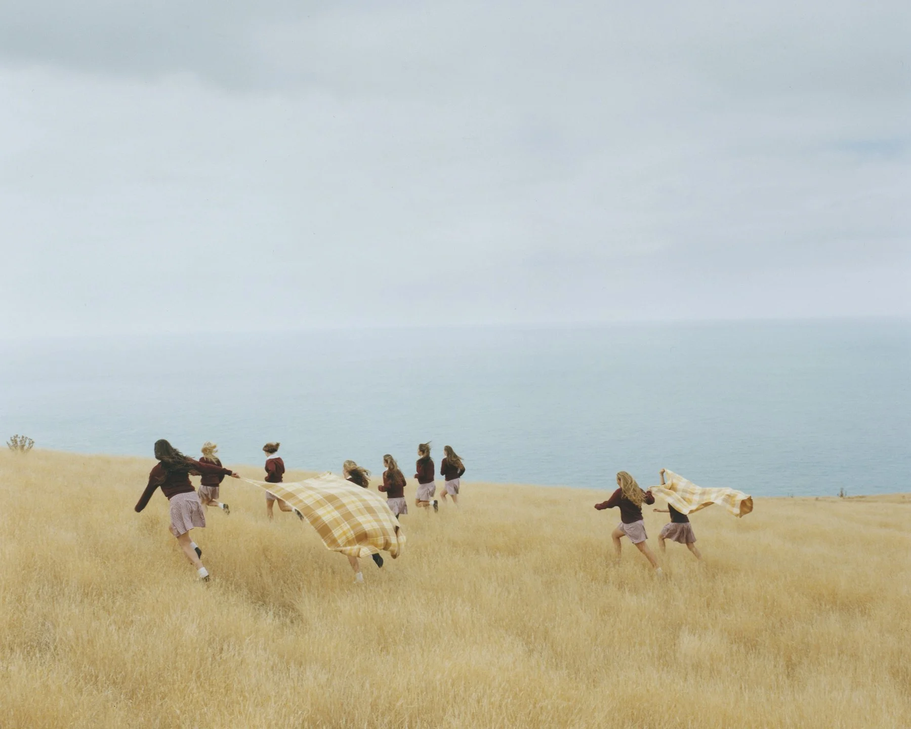 Group of people running and playing in a grassy field near the ocean on a cloudy day.