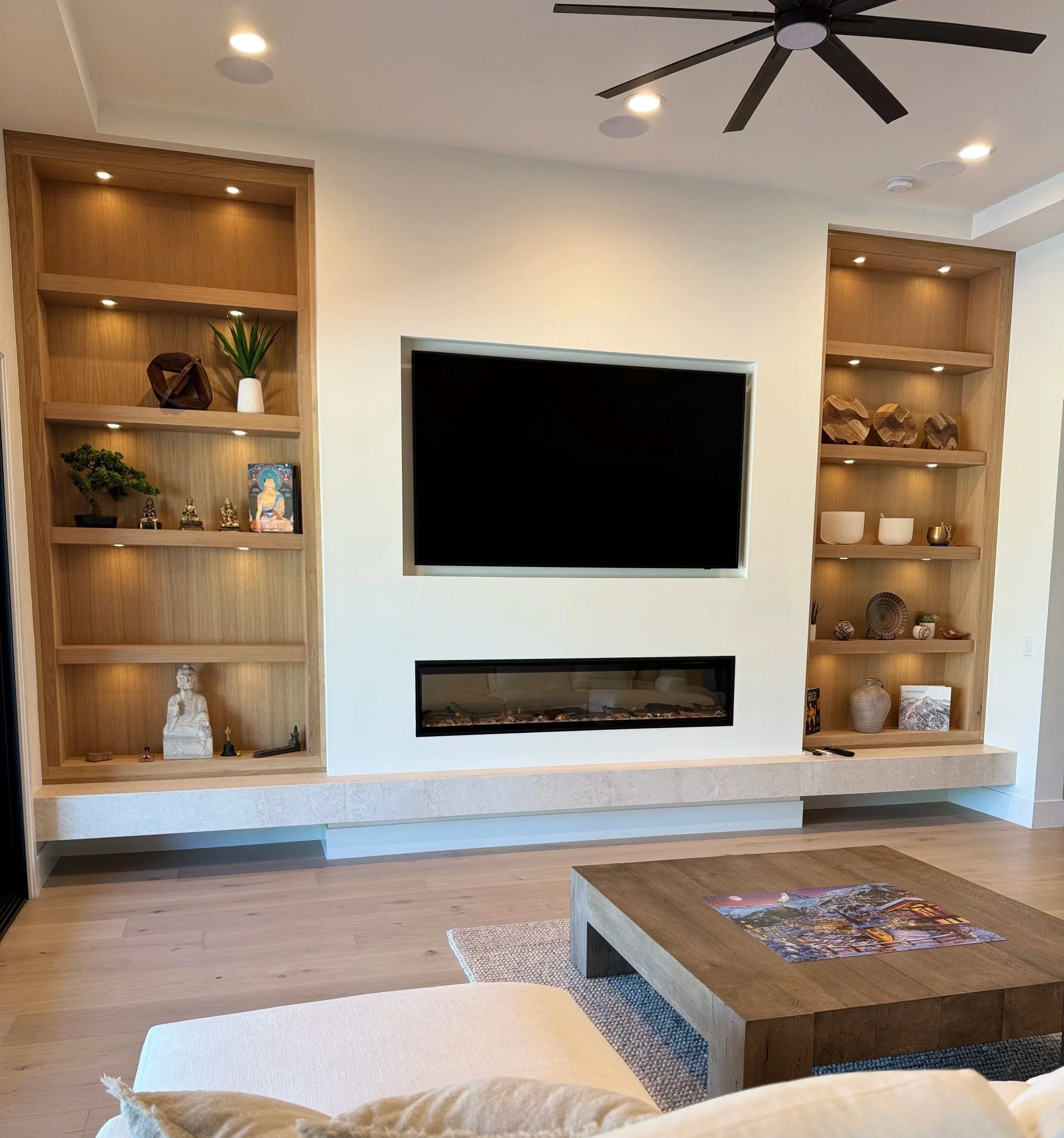 massive media wall 12 feet tall and 22 feet wide with massive white oak shelving with lighting, custom TV inset with a linear electric fireplace and stone slab bench seat in queen creek az