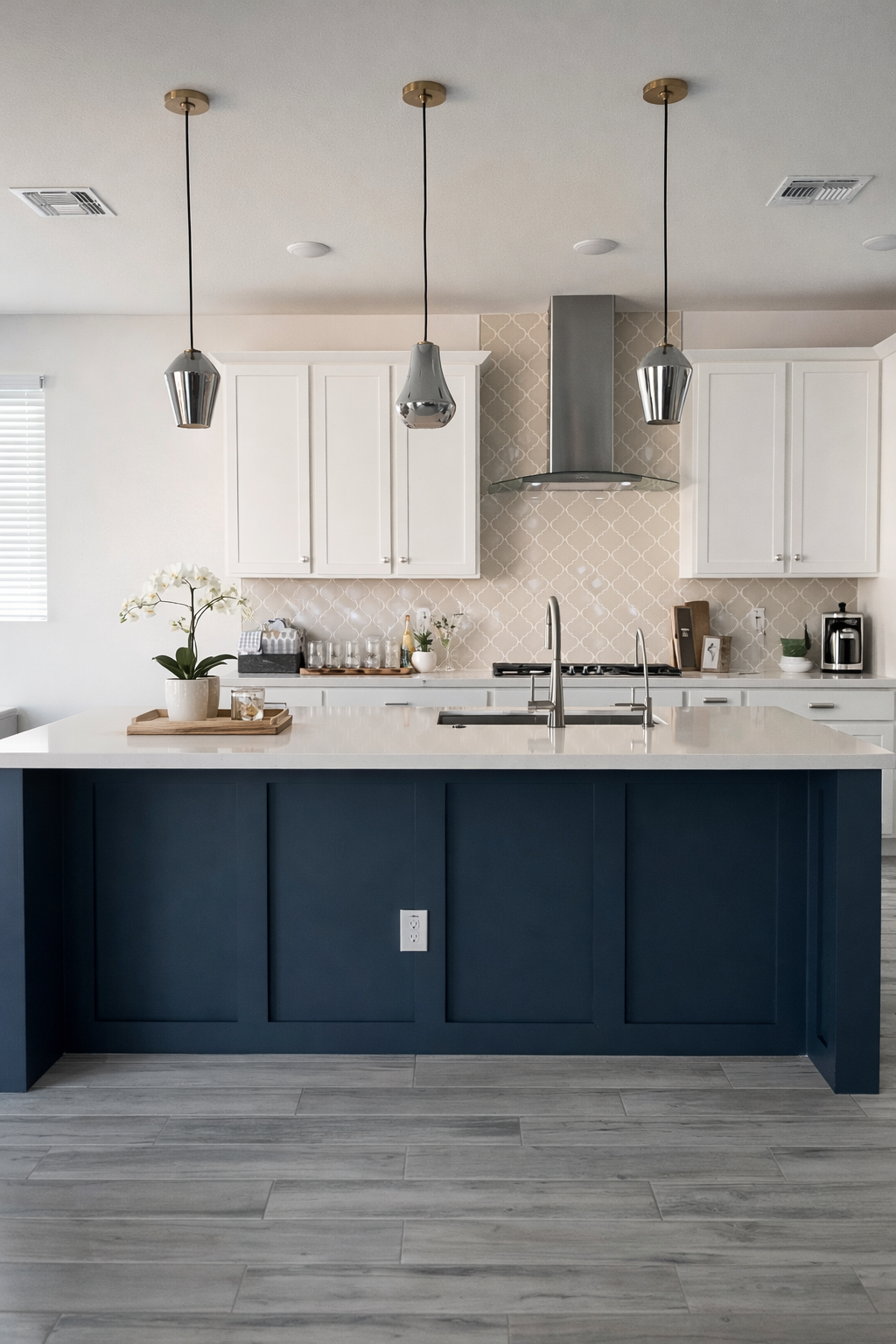 Modern kitchen with white cabinets, a navy blue island with white countertop, pendant lighting, and a patterned beige backsplash.